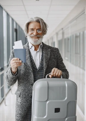 A man smiling, holding a passport and a travel bag.