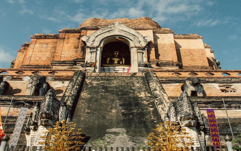 The front view of Wat Chedi Luang, a grand Buddhist temple, shows devotees praying in a peaceful setting.